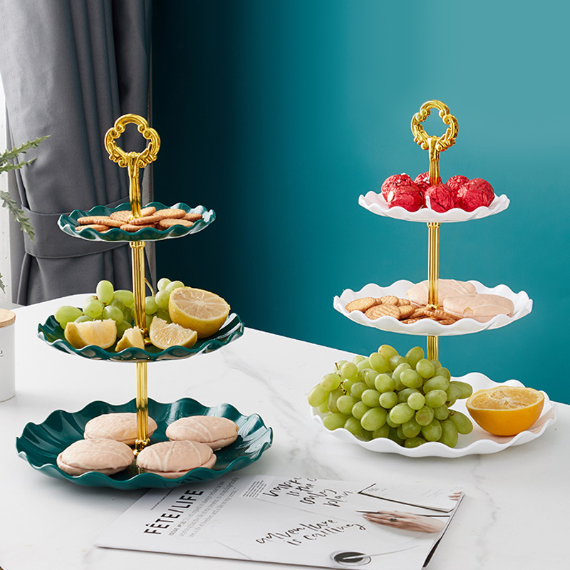 Teal three-tier stand with gold handle filled with biscuits, grapes and lemon slices