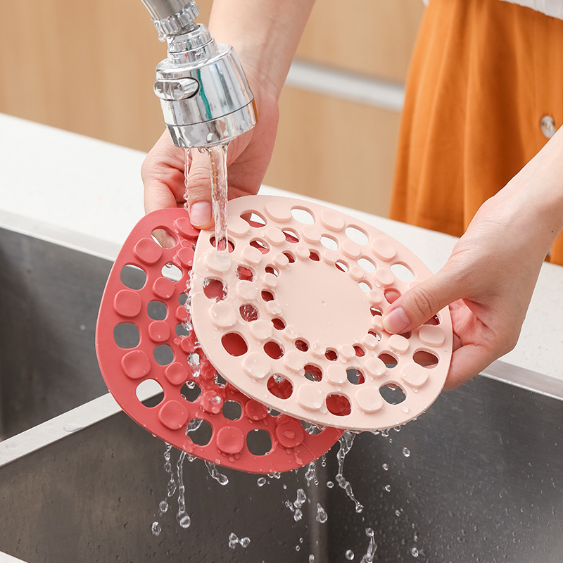 Hands rinsing silicone table mats under a running tap at the sink