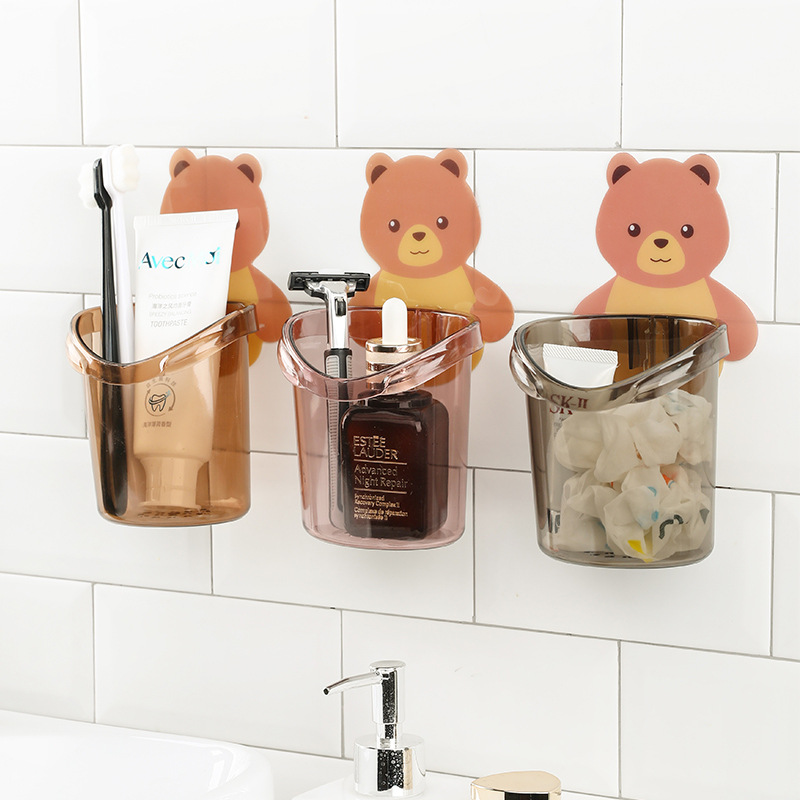 Three bear wall cups holding toothbrushes and a razor on a tiled wall
