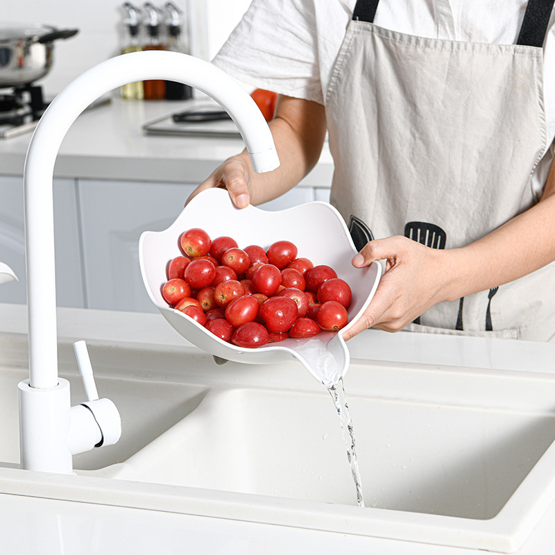 Hands rinsing grape tomatoes in a white petal bowl with water draining from the corner