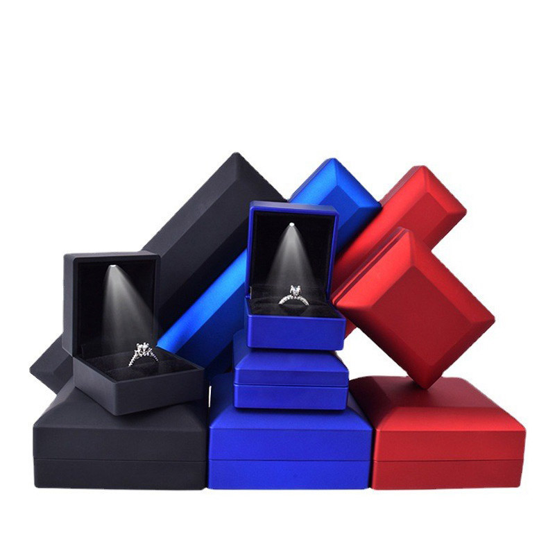 Matte black, blue and red jewelry boxes open, showing lit velvet interiors