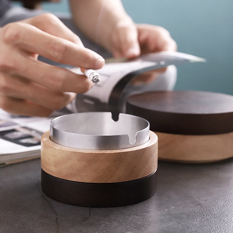 Hand tapping a cigarette over a steel ashtray on a grey table