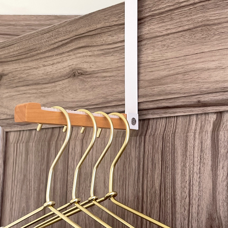 Gold hangers hanging from a wood bar on a white over-door hook