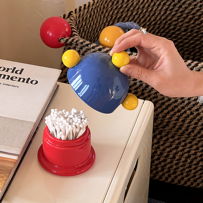 Red swab cylinder with white swabs on a cream nightstand beside a lifted lid