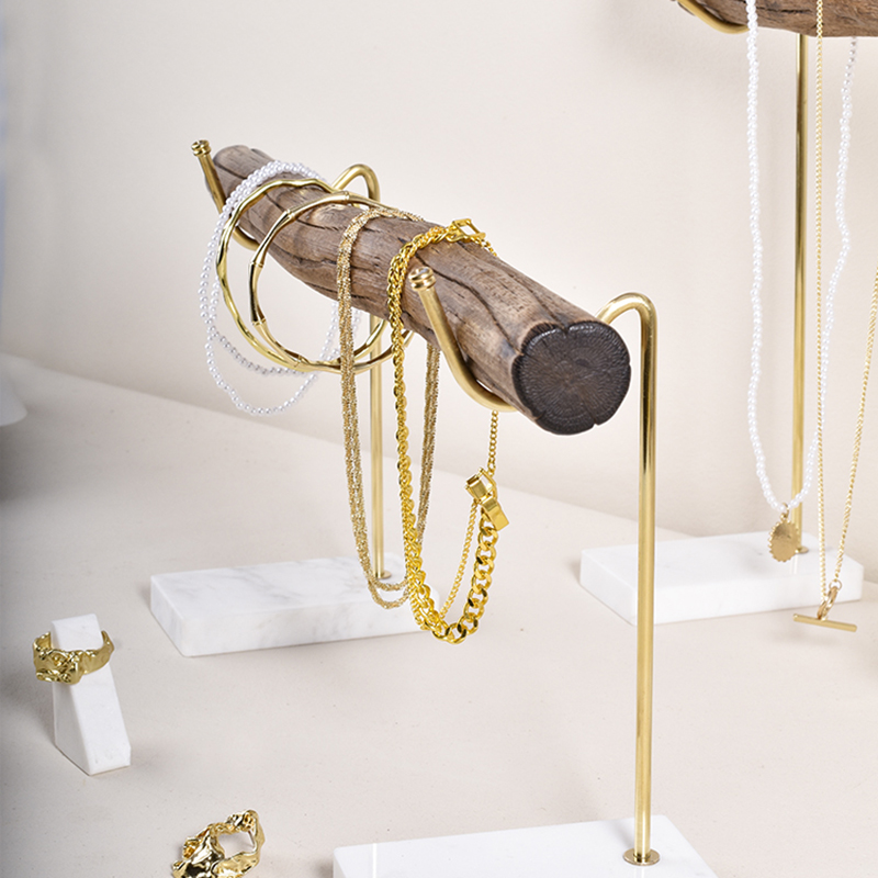 Gold necklaces hanging on separate brass hooks along a wooden crossbar