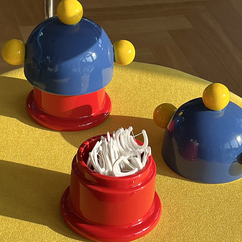 Red cylinder holding white dental floss beside a blue domed lid