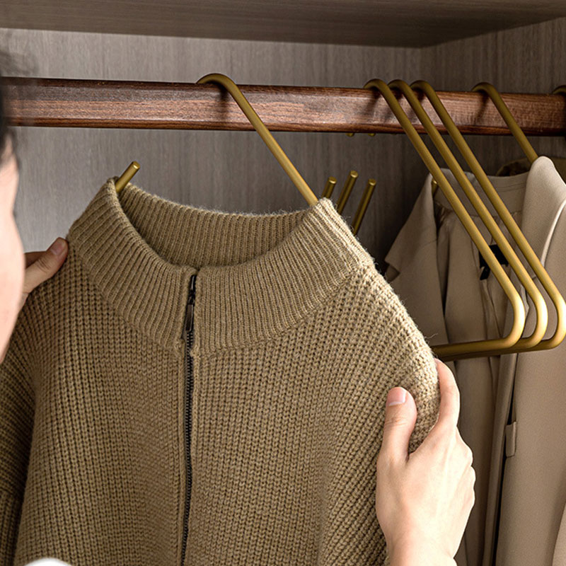 Hand placing a brown zip sweater on gold hangers in a wardrobe