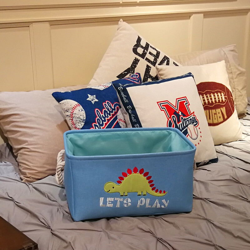 Sky blue dinosaur toy basket with rope handle set on a bed among pillows