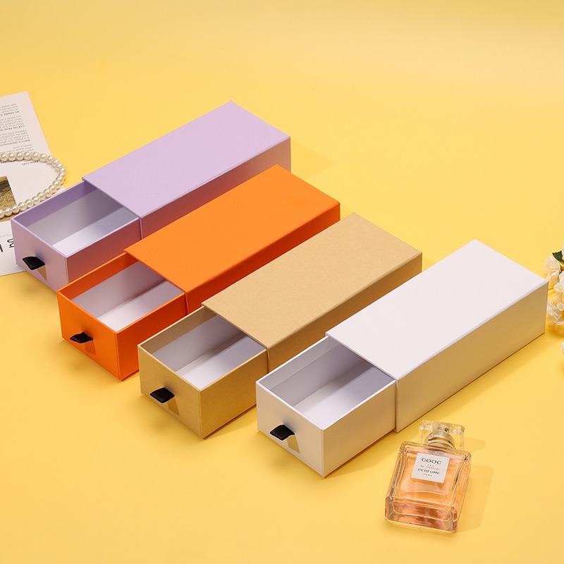 Matte drawer box with black ribbon pull set beside a perfume bottle