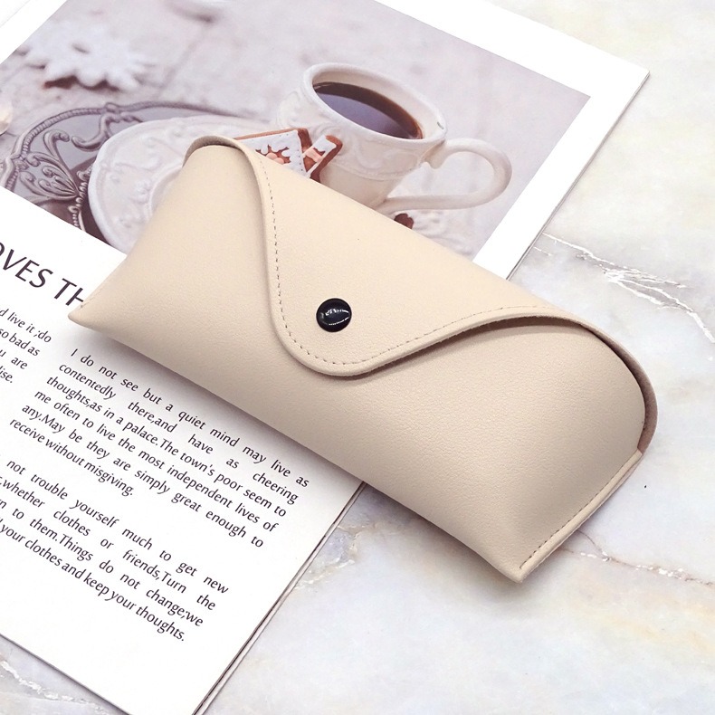 Beige glasses case resting on a marble surface beside a magazine and cup
