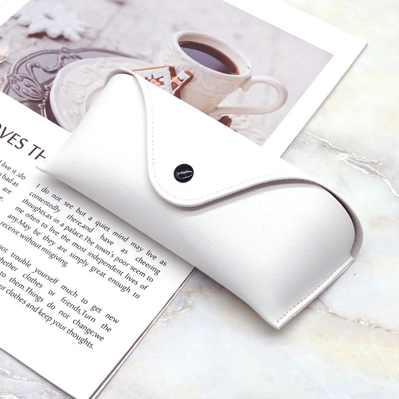 White glasses case with flap and stitching resting on an open magazine