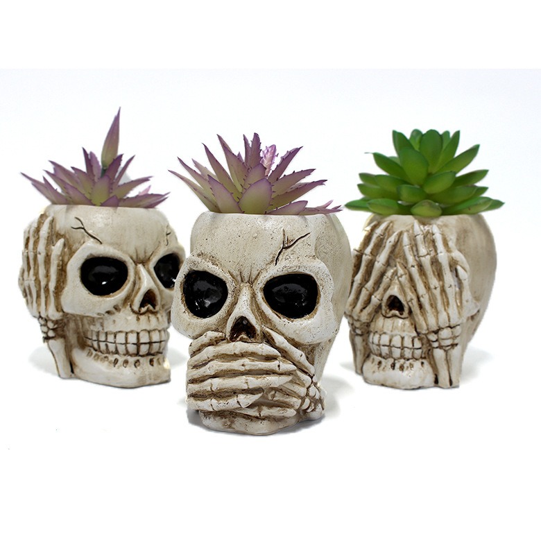 Three skull planters with distinct hand poses lined up together