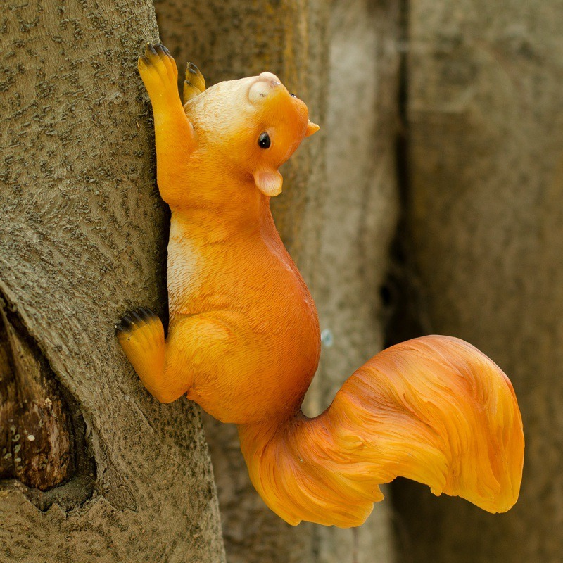 Orange resin squirrel gripping tree bark with its tail curling outward
