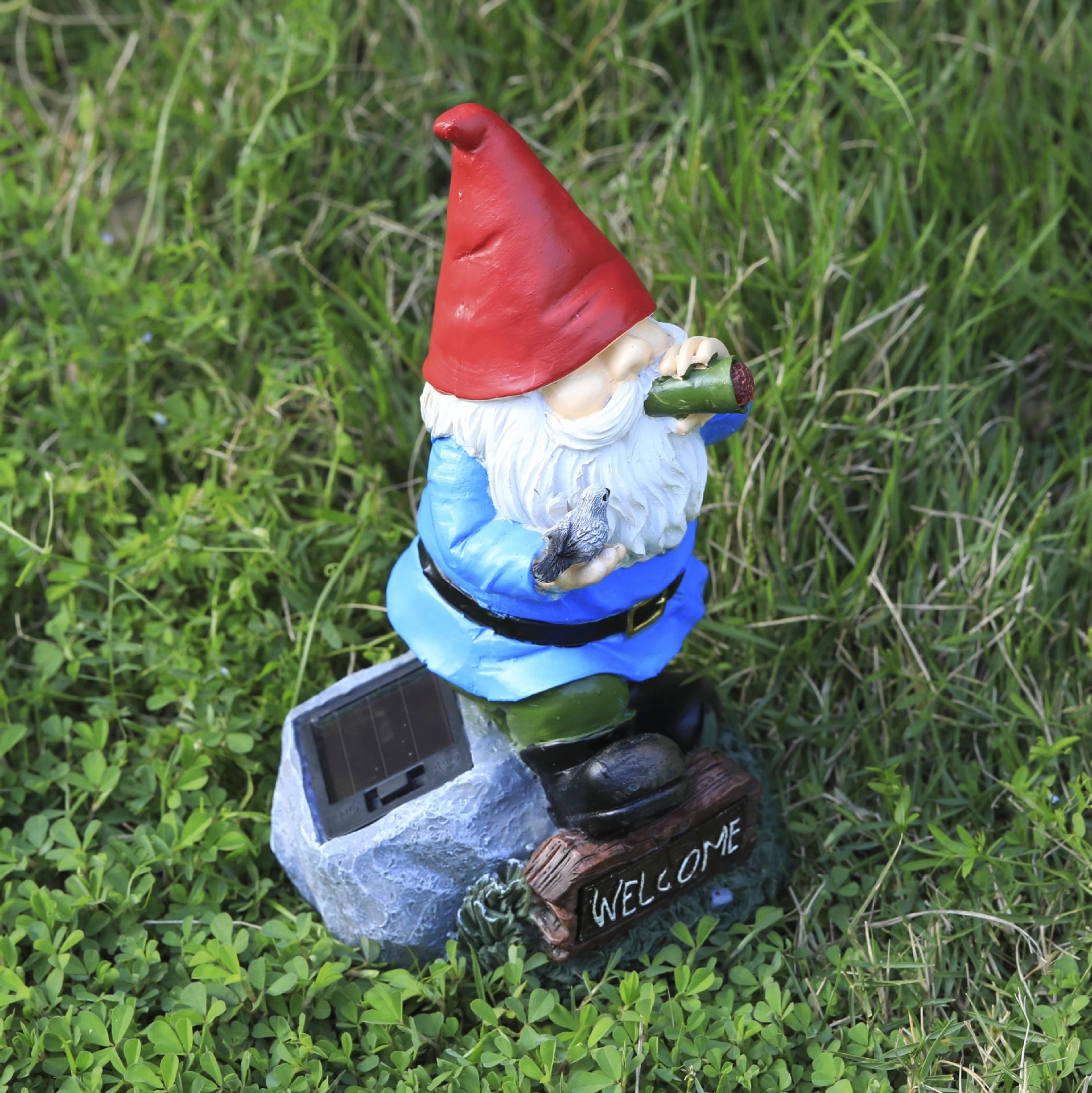 Gnome with WELCOME sign standing in green grass in front of a garden