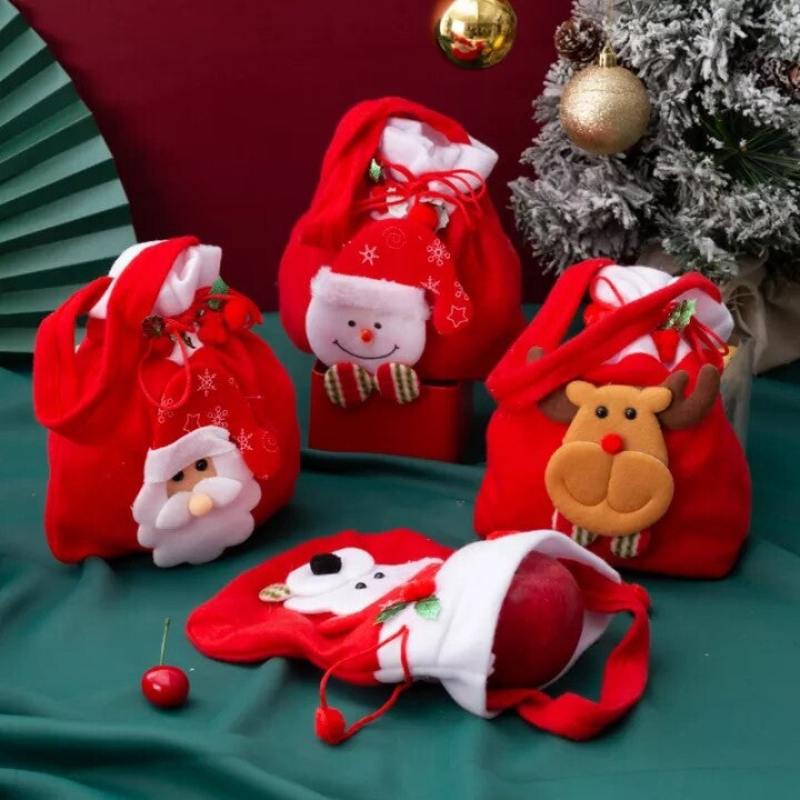 Four Christmas gift bags on green cloth beside a flocked tree