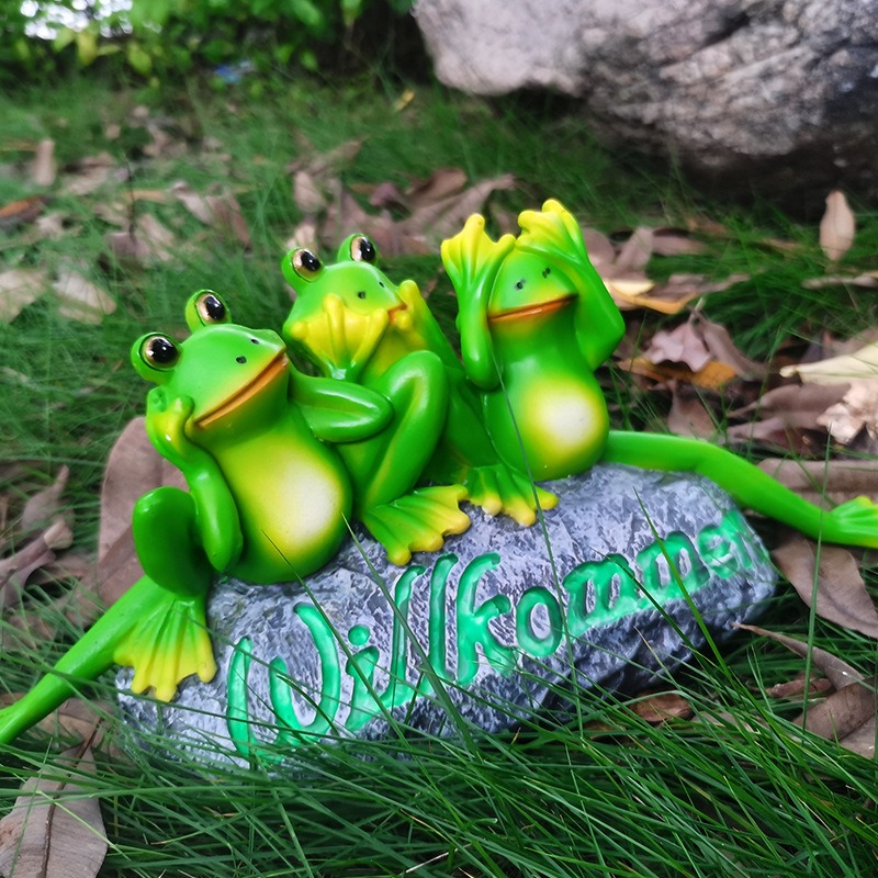 Frog welcome stone sitting in green grass beside fallen leaves