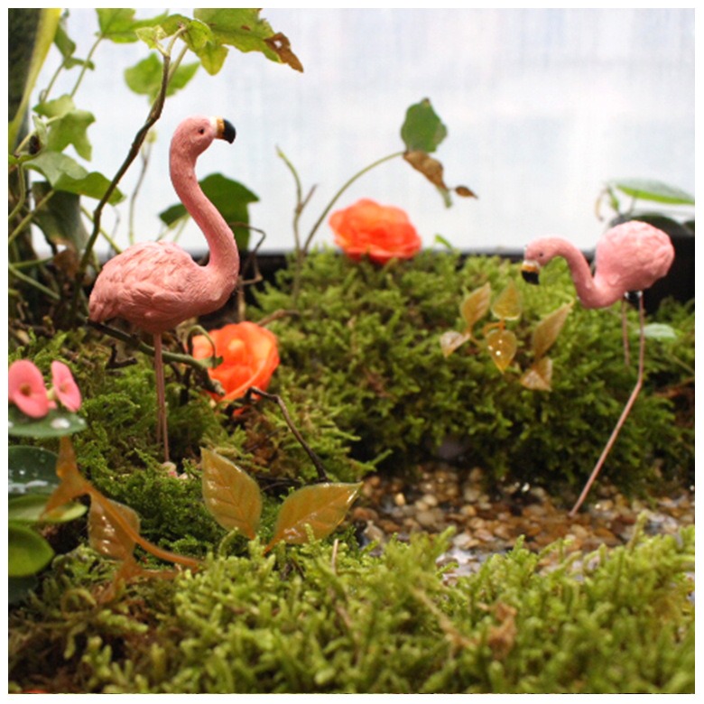 Miniature flamingos placed among moss, roses and pebbles in a terrarium