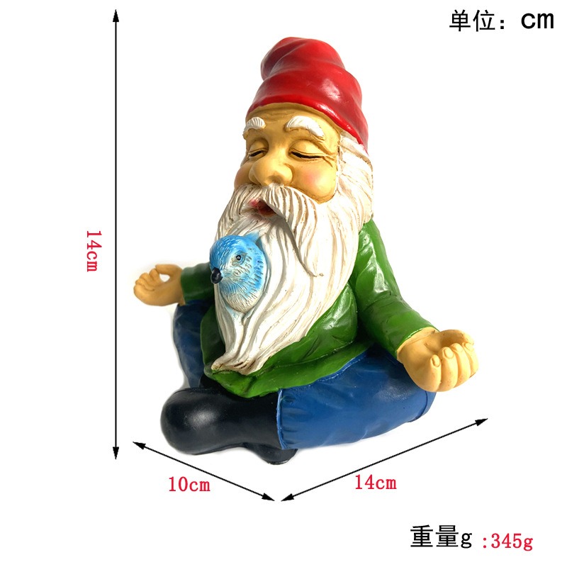 Meditating resin gnome seated in a garden setting beside a fairy garden