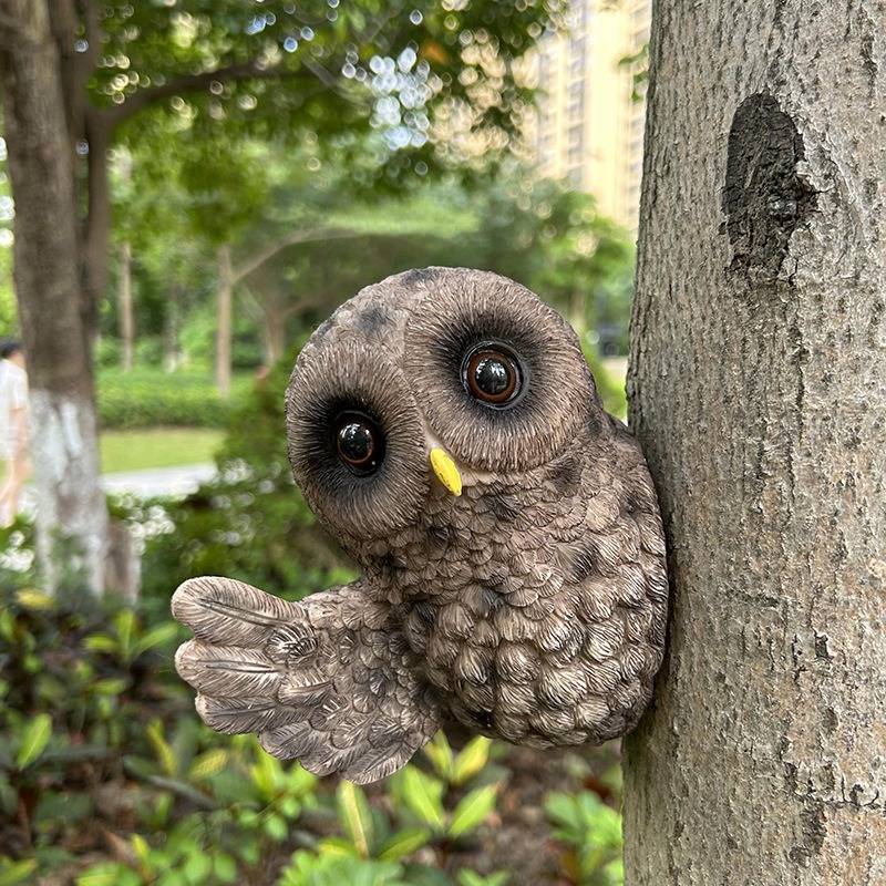 Resin owl peeking from the side of a tree trunk in a garden