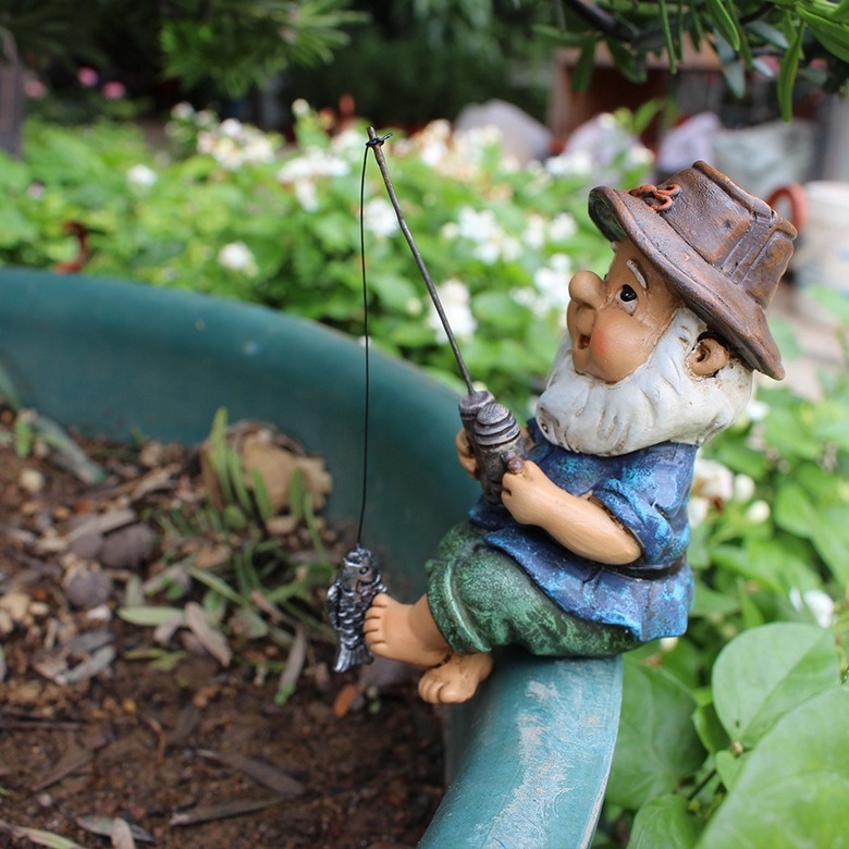 Fishing gnome perched on a planter rim among garden flowers