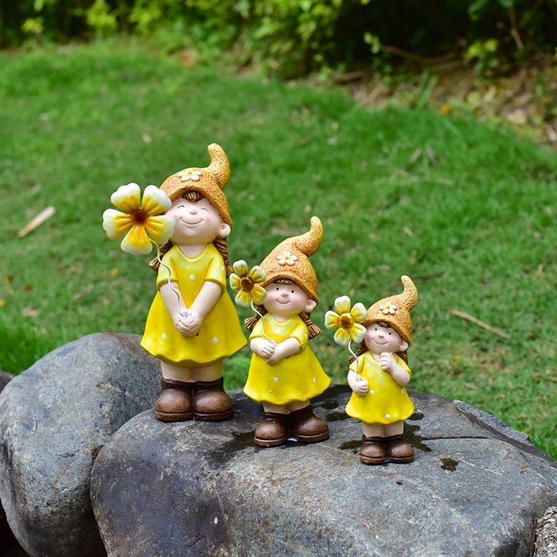 Three yellow girl garden figurines posed on a mossy rock with lawn behind