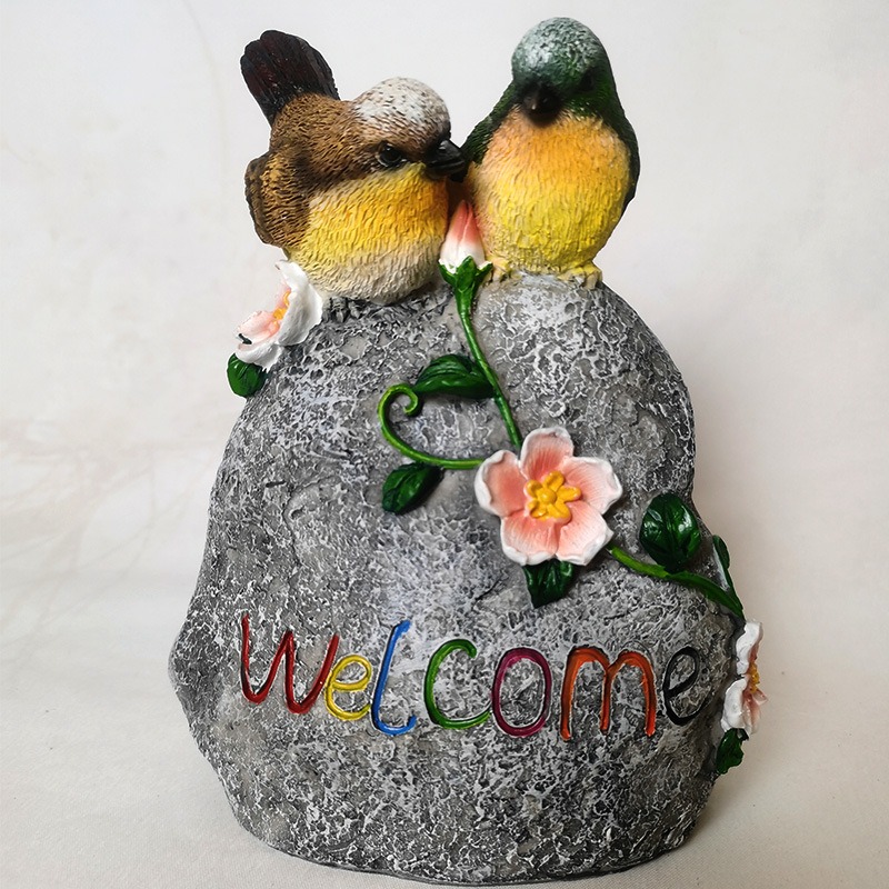 Two resin songbirds and pink blossoms on textured stone, close up