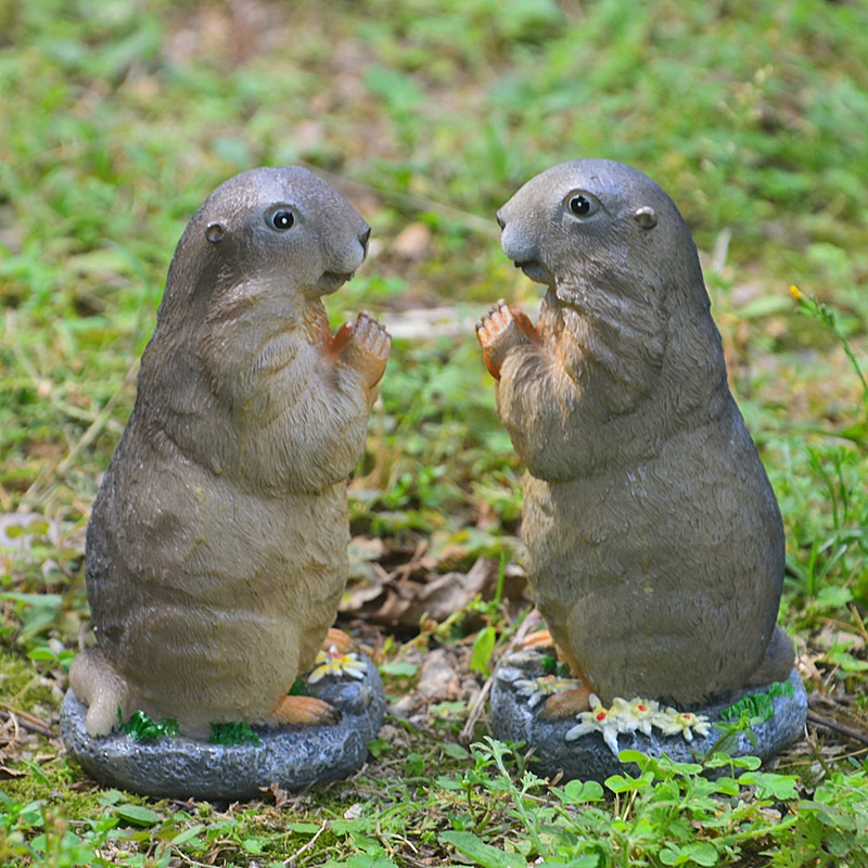 Two groundhog figurines in side view on stone bases among grass