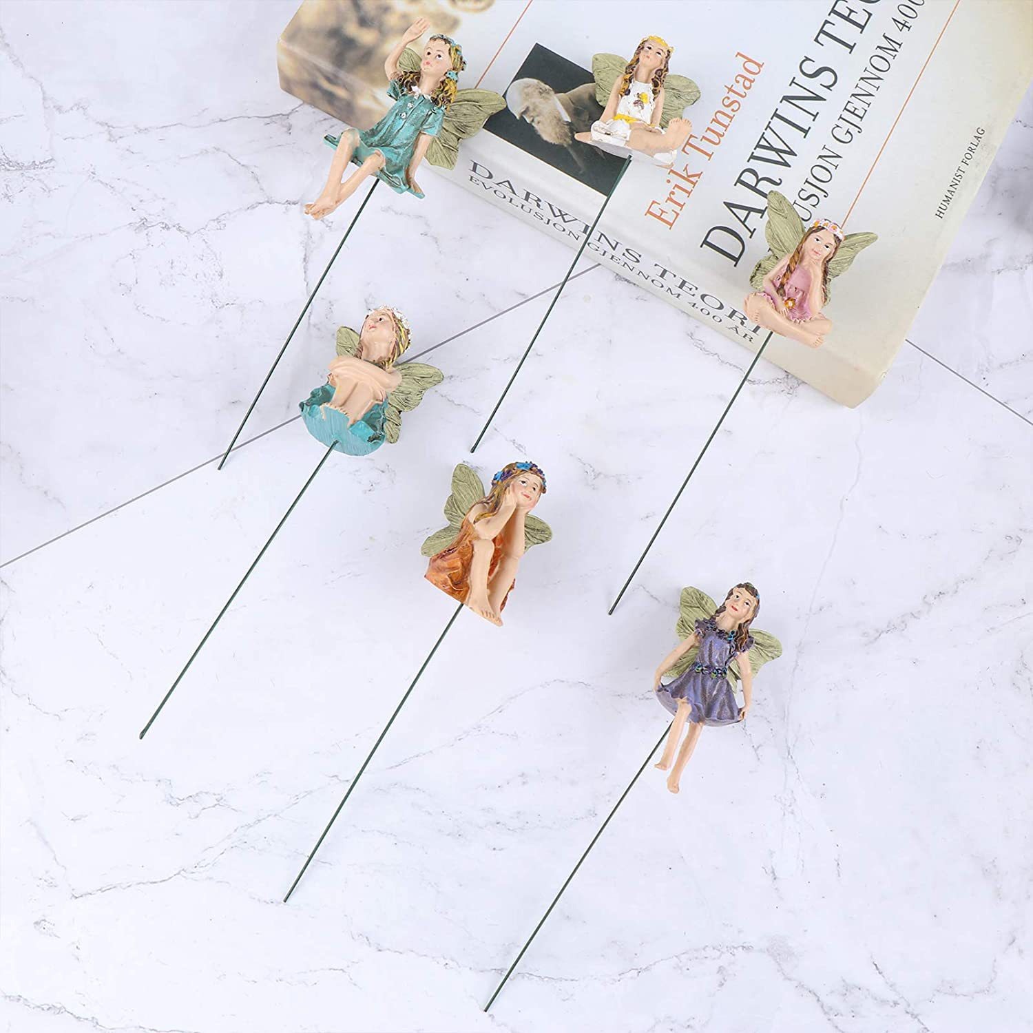 Fairy figures on a marble surface beside a book, showing scale