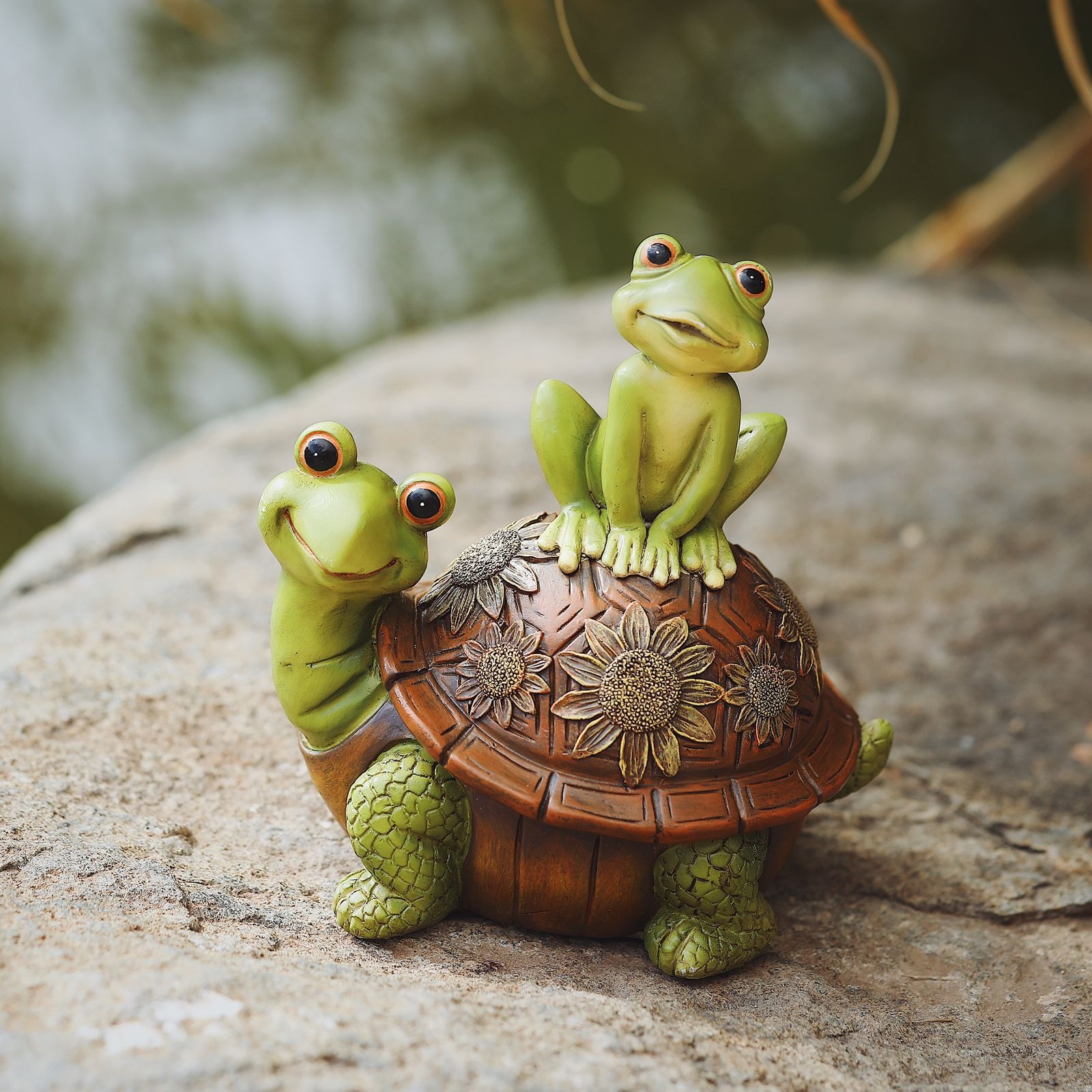 Frog and turtle statue resting on a rock outdoors among greenery