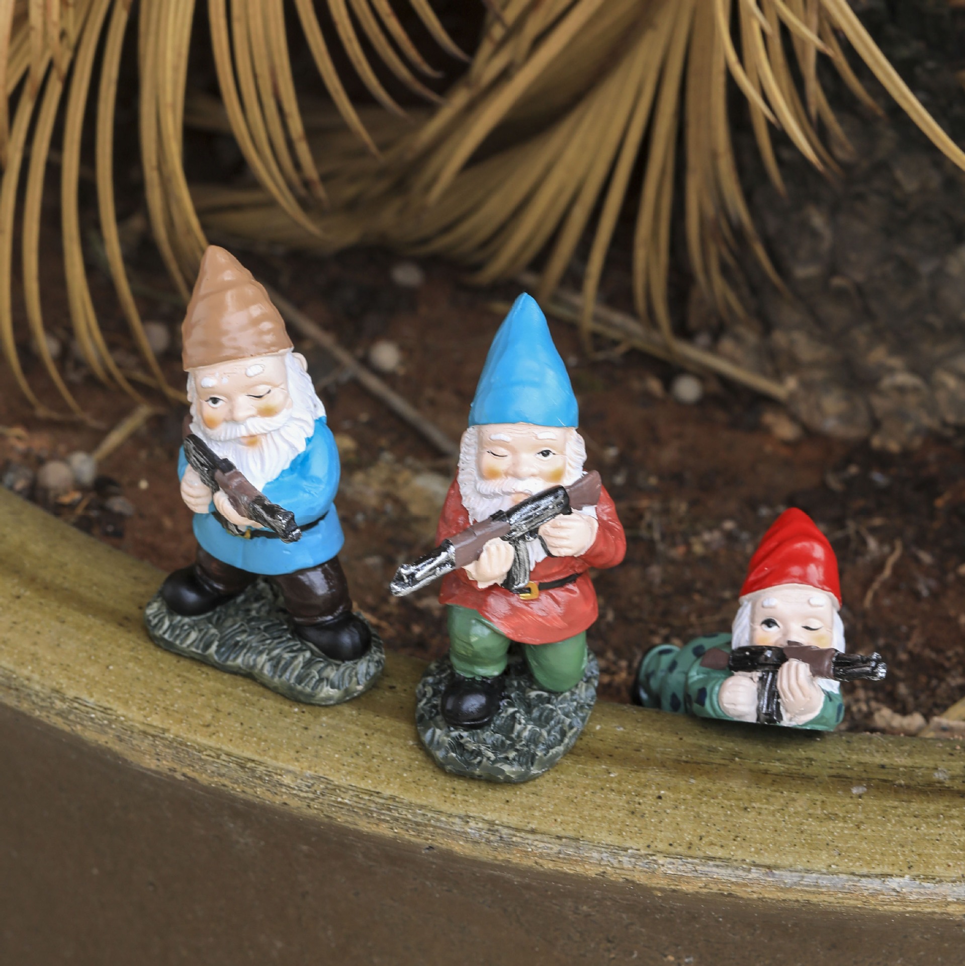 Three gnomes in varied poses on a planter edge with palm fronds behind