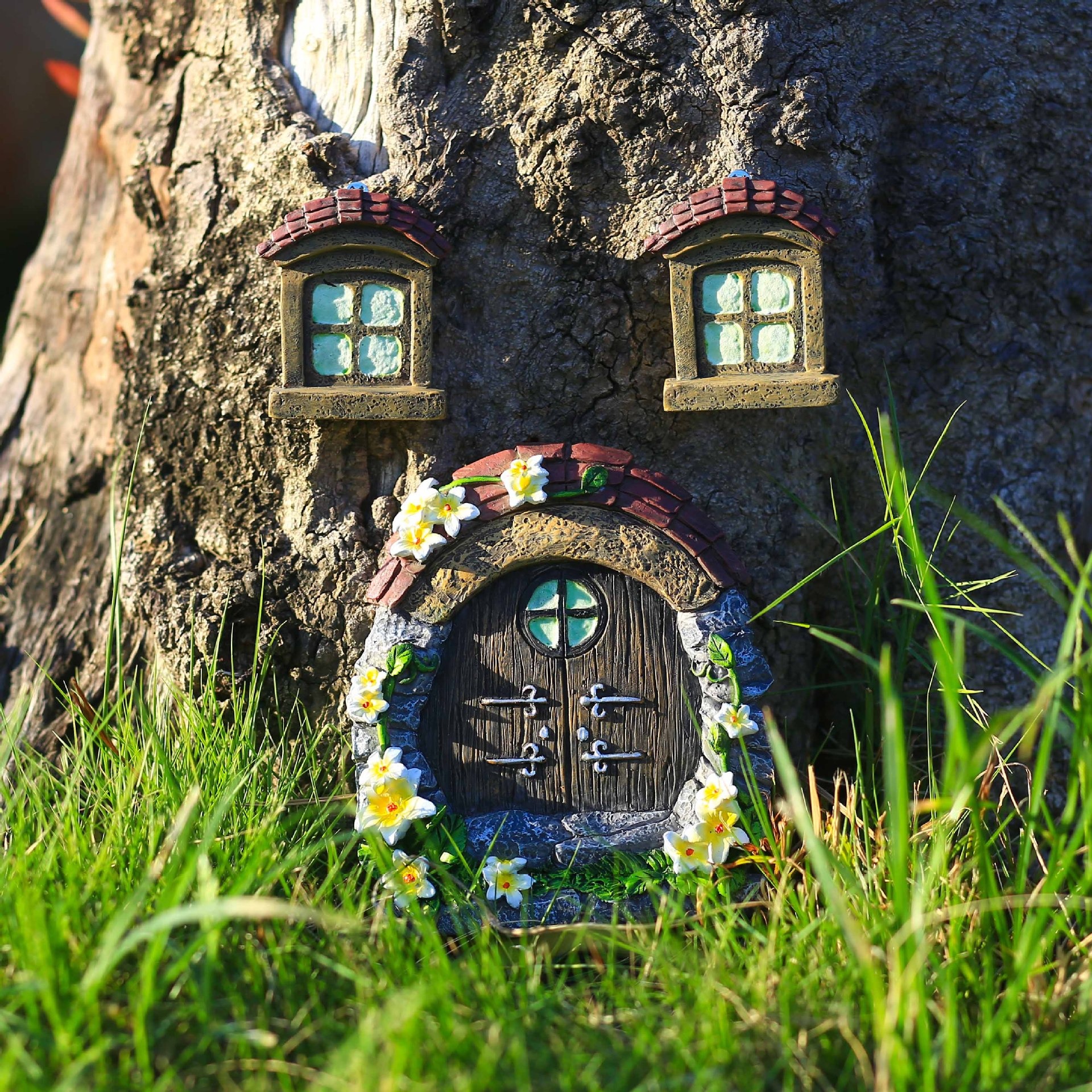 Fairy door and two windows mounted on a tree trunk in green grass