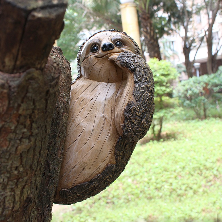 Resin sloth mounted on a tree trunk outdoors in a garden