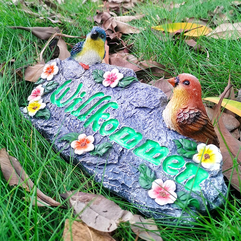 Welcome stone set in grass among leaves with green lettering visible