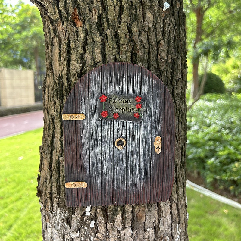 Close-up of arched resin fairy door with plaque and gold hinges