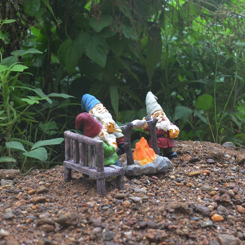 Two gnomes at a campfire among leaves and pebbles outdoors