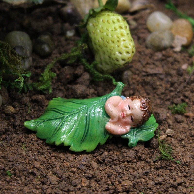 Sleeping fairy figurine on soil beside a small resin strawberry
