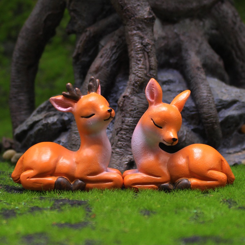 Stag and doe figurines resting together on moss near a tree root backdrop