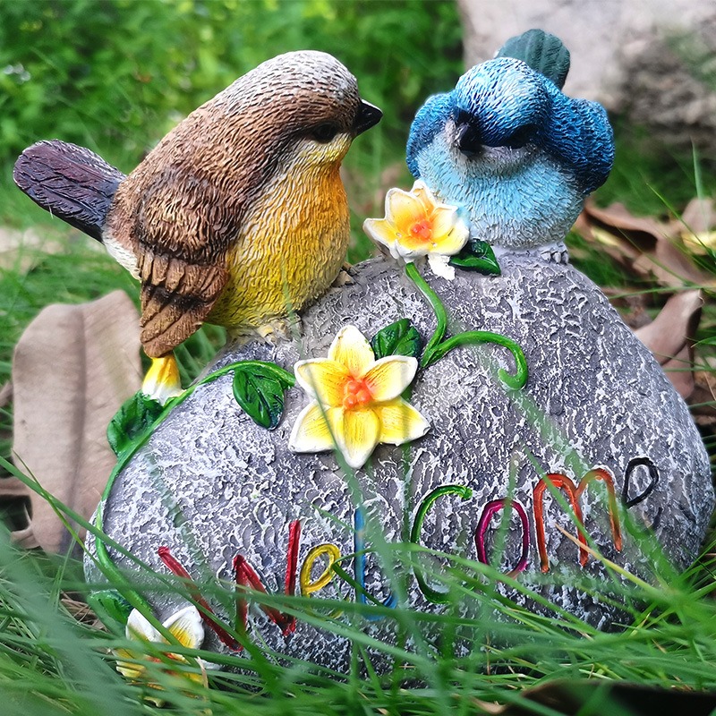 Resin garden bird ornament sitting on grass with fallen leaves