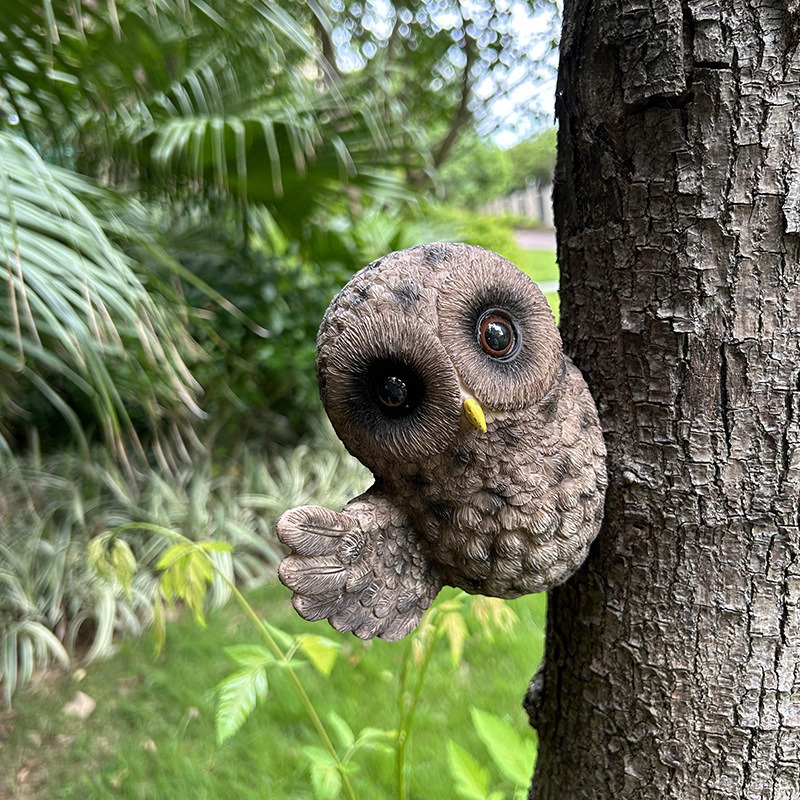 Side view of resin owl on a tree trunk with plants below