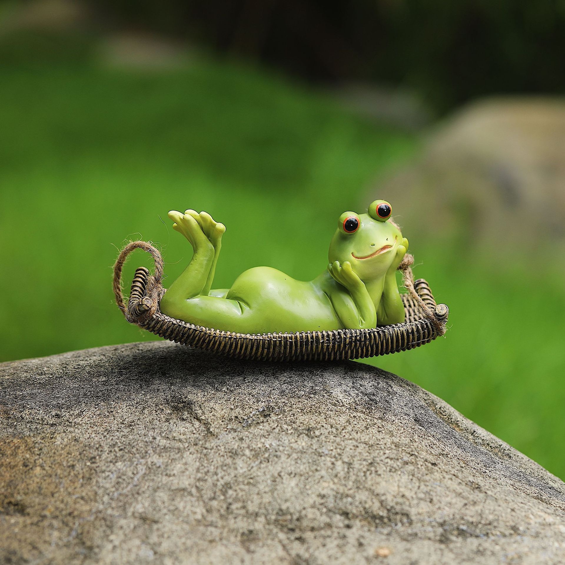 Frog swing figurine sitting on a garden rock beside a green lawn