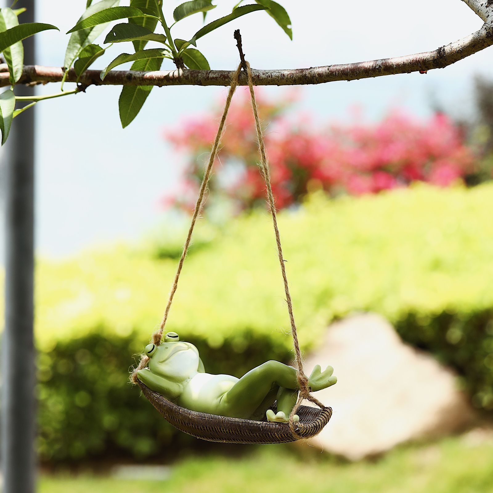 Frog figurine swinging from a tree branch with leaves behind it