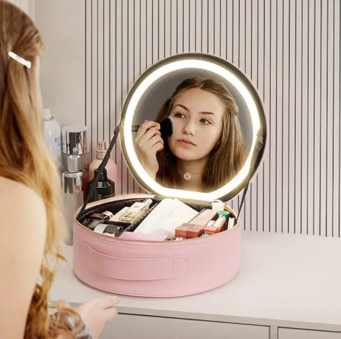 Woman using lit mirror on pink makeup case at a vanity table