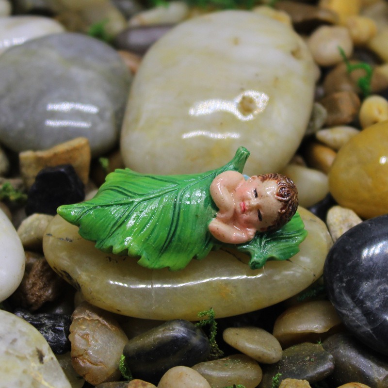 Fairy figurine resting on a smooth pebble among moss and colorful stones