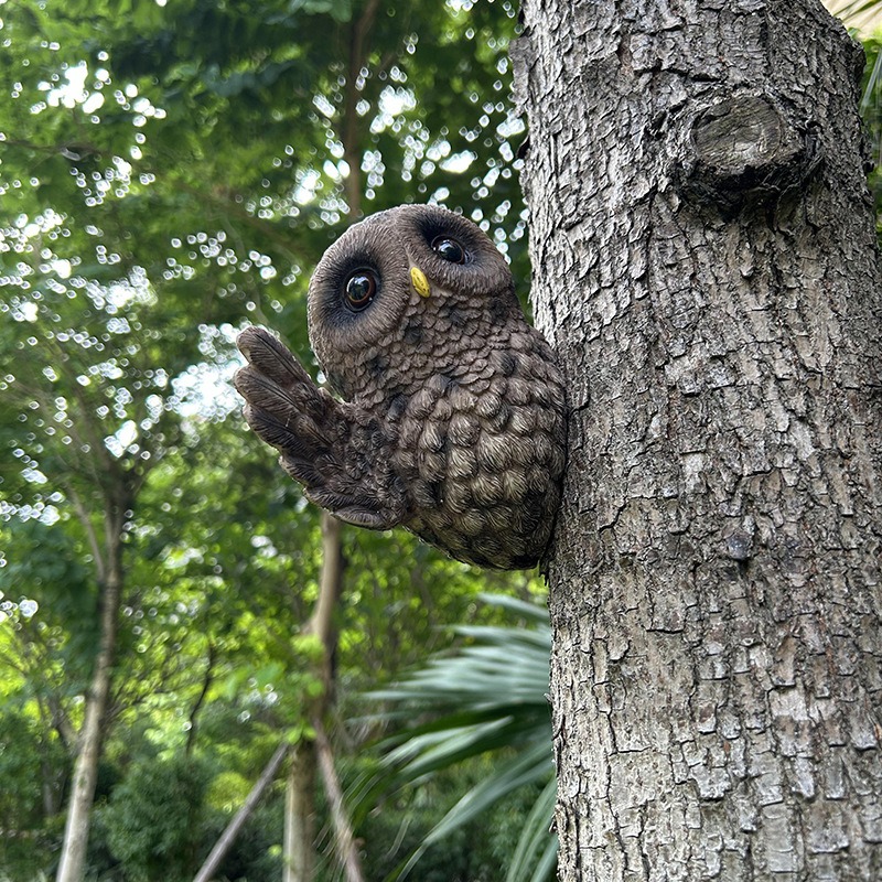 Resin owl ornament clinging to a tree trunk in a green garden