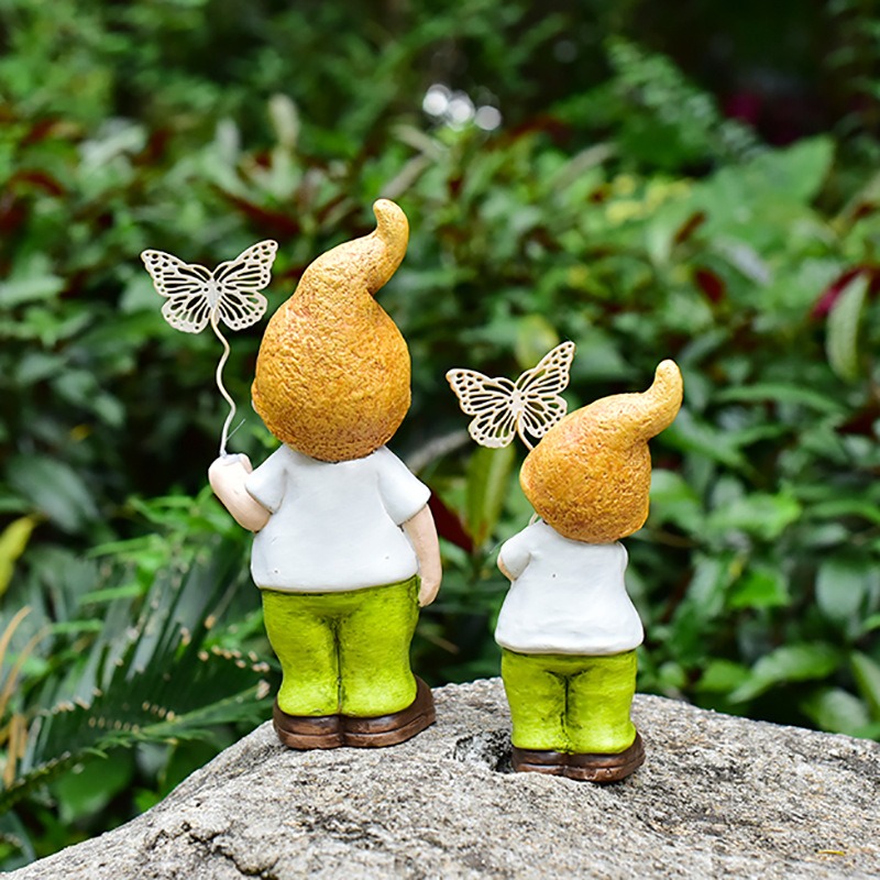 Back view of dwarf figurines with metal butterfly wands on rock