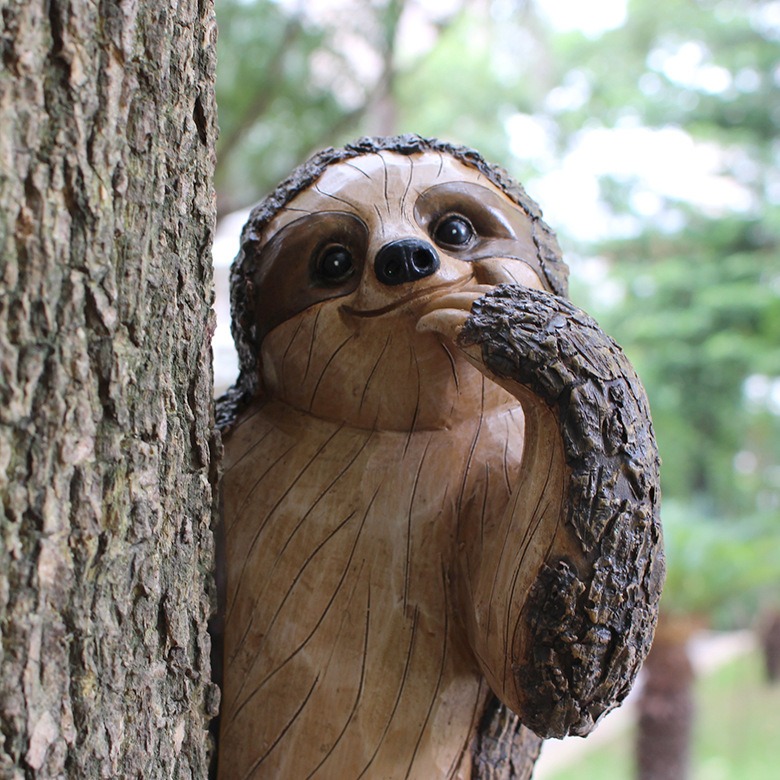 Resin sloth clinging to a tree trunk beside greenery