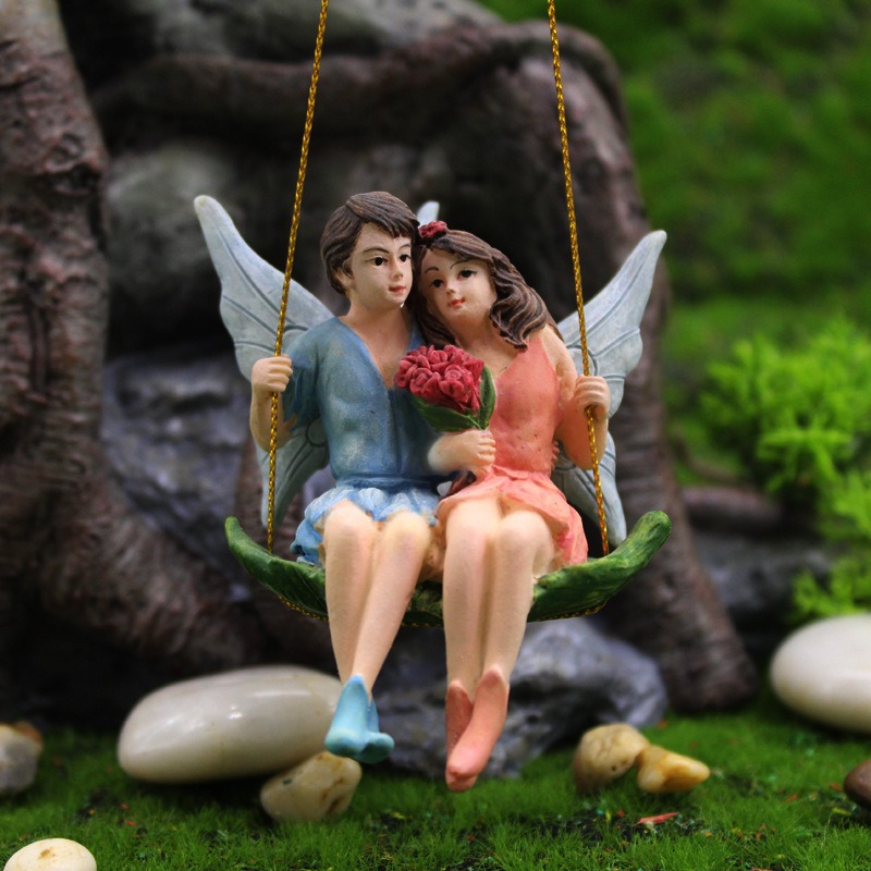 Fairy couple swing pendant displayed among stones and moss in a miniature garden