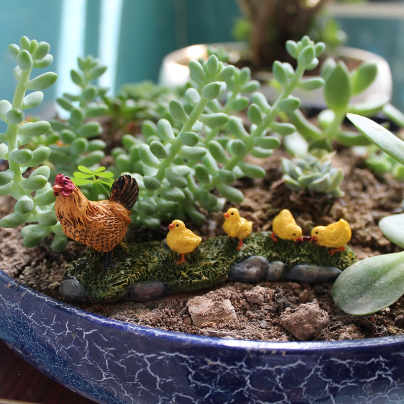 Miniature hen and chicks figurine sitting among succulents in a planter