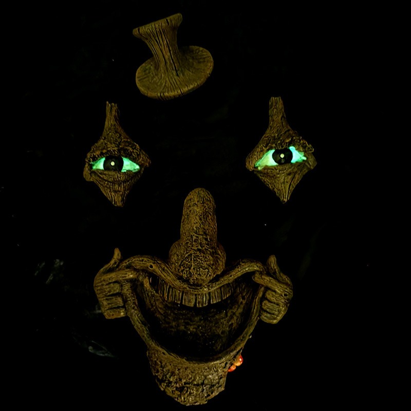 Tree face ornament in darkness with glowing green eyes