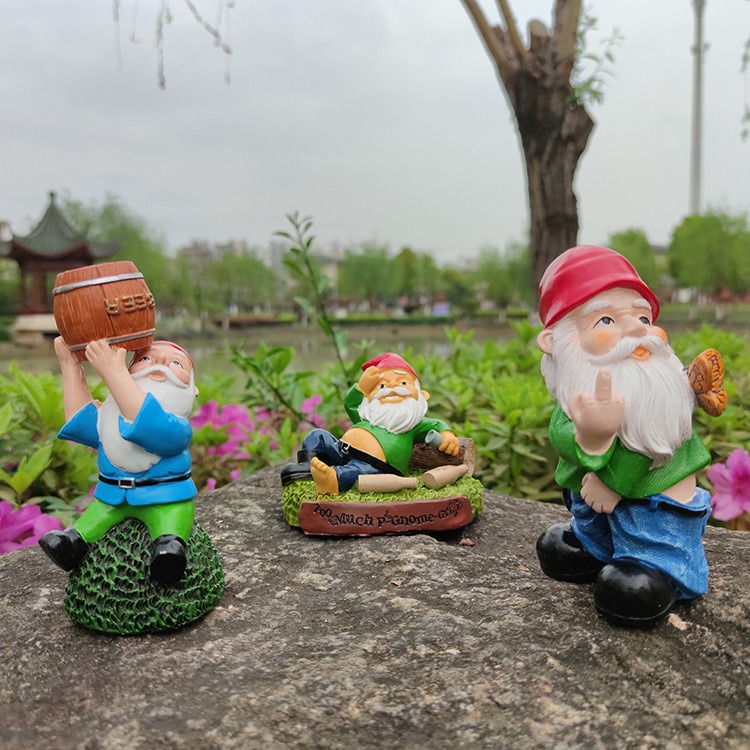 Three resin gnome figurines on a rock outdoors with varied poses